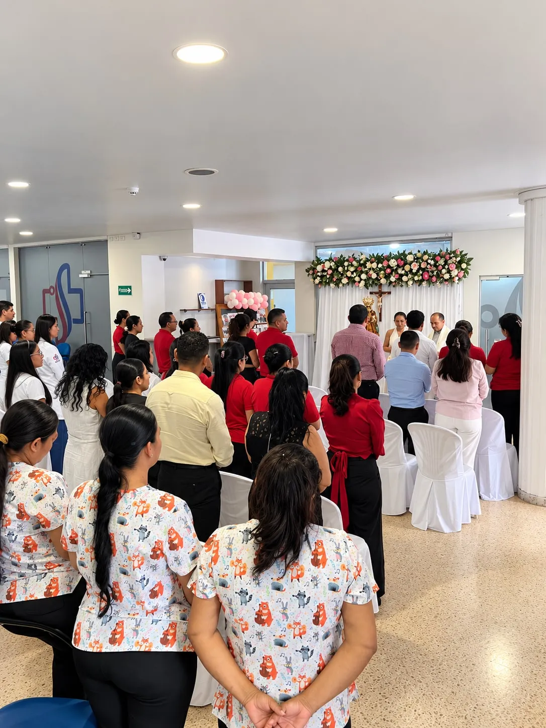 El personal del hospital reunido en el vestíbulo, en una ceremonia frente a un altar con flores.